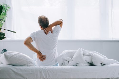 back view of man sitting on bed and suffering from back pain back view of man sitting on bed and suffering from back pain